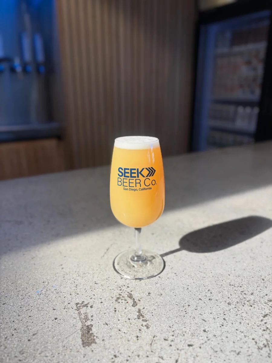 A hazy golden pour in a Seek Beer Co. glass on the bar
